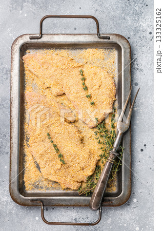 Cooking of Raw breaded Wiener Schnitzel steak in steel tray. gray background. top view Cooking of Raw breaded Wiener Schnitzel steak in steel tray. gray background. top view 133325162