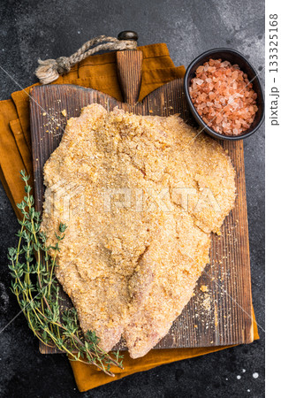 Wiener breaded raw pork Schnitzel, meat steak on a wooden board. black background. top view 133325168