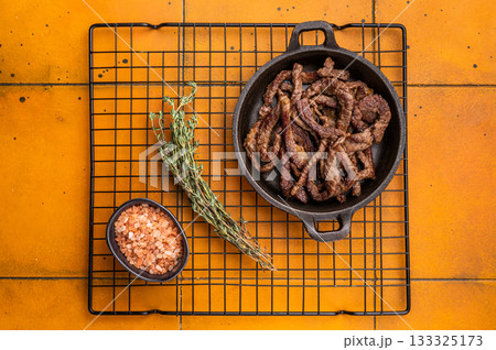 Fried beef tender strips, sliced steak in a skillet. orange background. top view 133325173