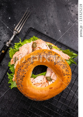 Bagel sandwich with lox, smoked salmon, lettuce and cream cheese on a rack. black background. top view Bagel sandwich with lox, smoked salmon, lettuce and cream cheese on a rack. black background. top view 133325219