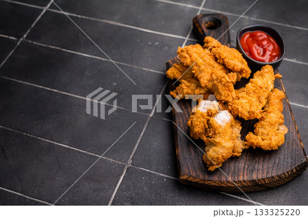 Fried chicken tenders or strips with hot sauce. black background. top view Fried chicken tenders or strips with hot sauce. black background. top view 133325220