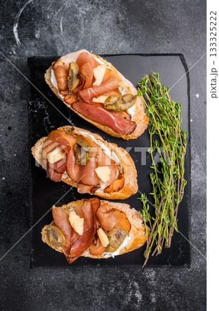 Prosciutto and pesto bruschetta, parmesan cheese and olives. black background. top view 133325222