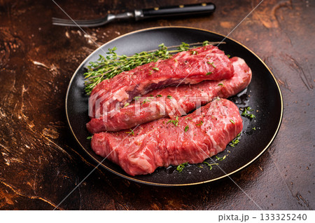 Tri tip steaks, Raw marbled beef meat on plate with herbs. brown background. top view 133325240