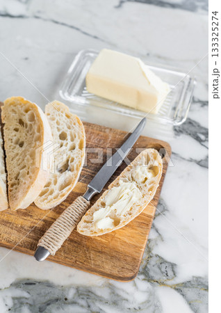 Sliced ciabatta bread with fresh butter on a wooden cutting board. marble background. top view 133325274