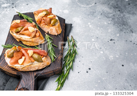 Tapa with Jamon cured ham, parmesan cheese and olives. grey background. top view Tapa with Jamon cured ham, parmesan cheese and olives. grey background. top view 133325304