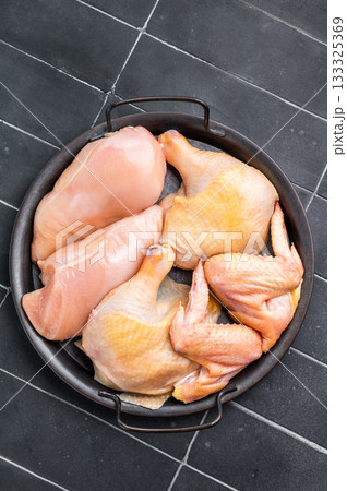 A black metal dish with a handle holds several pieces of fresh, raw chicken. The chicken is arranged neatly in the dish A black metal dish with a handle holds several pieces of fresh, raw chicken. The chicken is arranged neatly in the dish 133325369