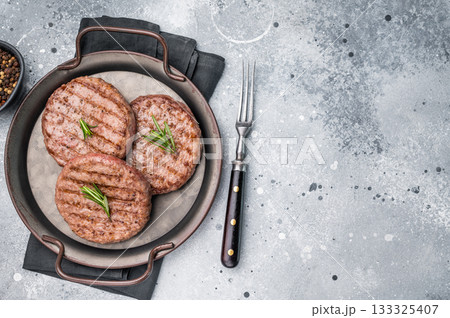 Close up of a flavorful grilled beef meat patty, ready to be topped with fresh ingredients for a delicious meal. grey background. top view 133325407