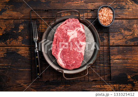 Prime Rib eye steak in a tray, raw dry aged beef meat on wooden background. top view Prime Rib eye steak in a tray, raw dry aged beef meat on wooden background. top view 133325412