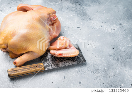 A whole raw chicken and some chicken parts sit on a cutting board with a knife A whole raw chicken and some chicken parts sit on a cutting board with a knife 133325469