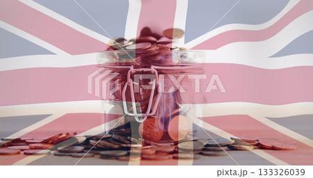 Displaying glass jar holding assorted coins on wooden tabletop, with Union Jack flag overlay 133326039