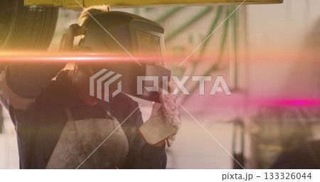 Female technician lifting welding helmet from vehicle in repair workshop, with gloves and apron Female technician lifting welding helmet from vehicle in repair workshop, with gloves and apron 133326044
