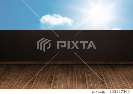 Empty wooden deck meeting dark tiled wall, bright sun shining near white cloud over blue sky Empty wooden deck meeting dark tiled wall, bright sun shining near white cloud over blue sky 133327360