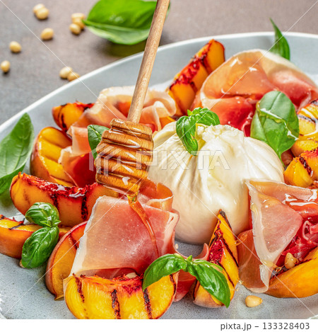 Burrata cheese with prosciutto, grilled peaches, honey and basil on plate, gourmet appetizer, close up 133328403