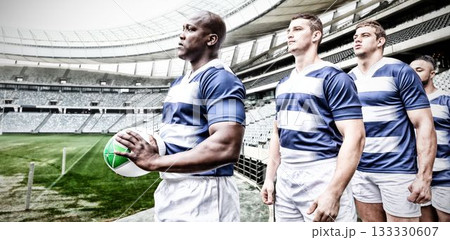 Multiracial male players with ball standing in a row and looking away at stadium 133330607