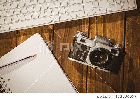 Vintage film camera is resting beside keyboard and notebook with pencil in flat design workspace Vintage film camera is resting beside keyboard and notebook with pencil in flat design workspace 133330957