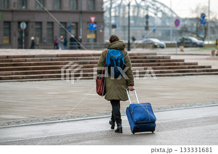 A tourist with a backpack pulls a suitcase on wheels down the street, rear view 133331681