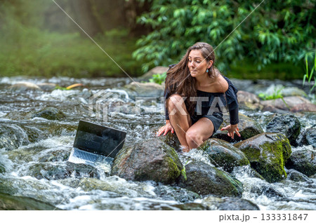 worried woman pulls out of water laptop that fell into river, remote holiday work accident 133331847