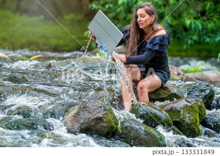 worried woman pulls out of water laptop that fell into river, remote holiday work accident 133331849
