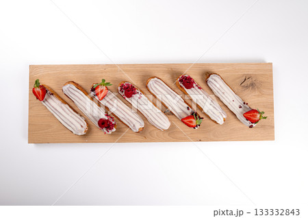 eclairs with glaze and strawberries on a wooden board, isolated on white, close-up, top view 133332843