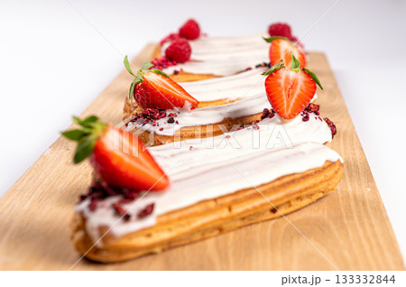 eclairs with glaze and strawberries on a wooden board, isolated on white, close up eclairs with glaze and strawberries on a wooden board, isolated on white, close up 133332844