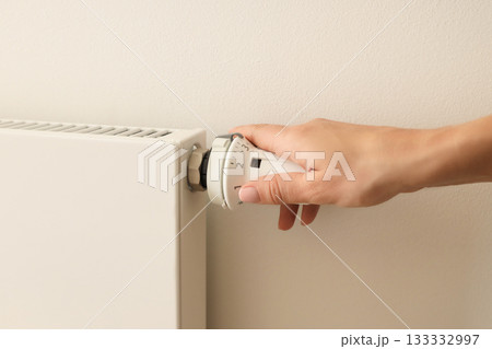 Hand is turning the thermostat on a radiator for warmth 133332997
