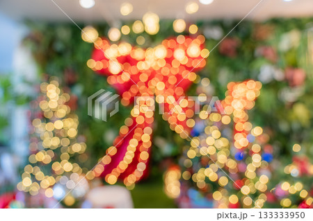 The image features blurred holiday lights forming round yellow and red bokeh shapes, with a large red bow and decorative trees soft in the background. The image features blurred holiday lights forming round yellow and red bokeh shapes, with a large red bow and decorative trees soft in the background. 133333950