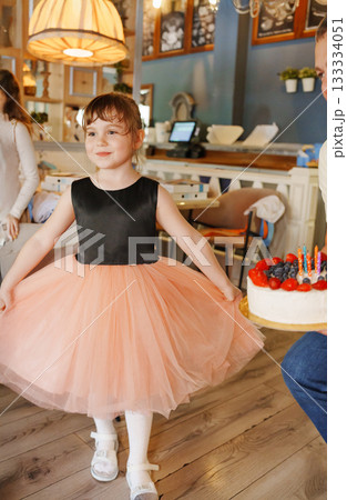 Girl in a black and pink dress holds cake in cafe 133334051