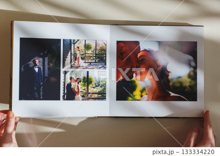 Female hands flipping through a photo book with wedding photos on a white table Female hands flipping through a photo book with wedding photos on a white table 133334220