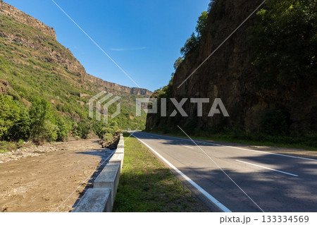 A winding road cuts through a canyon, flanked by tall rock walls and lush greenery 133334569