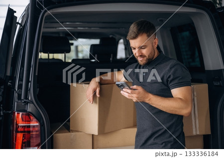 Using the smartphone. Delivery man or loader is near the car with a box 133336184