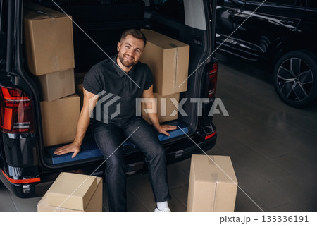 Taking a break, resting, sitting. Delivery man or loader is near the car with a box Taking a break, resting, sitting. Delivery man or loader is near the car with a box 133336191
