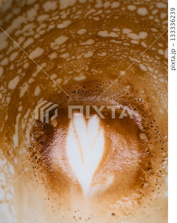 Close up of partially consumed cappuccino, showcasing fading heart shaped latte art design amidst creamy coffee foam and remnants of beverage. Heart shaped latte art fading within creamy coffee foam 133336239