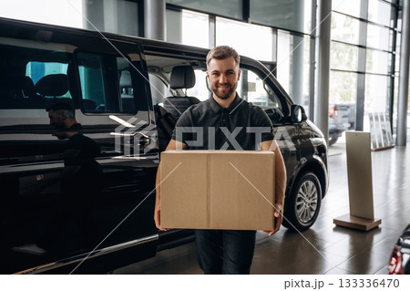 Big order, holding the box. Delivery man or loader is near the car with 133336470
