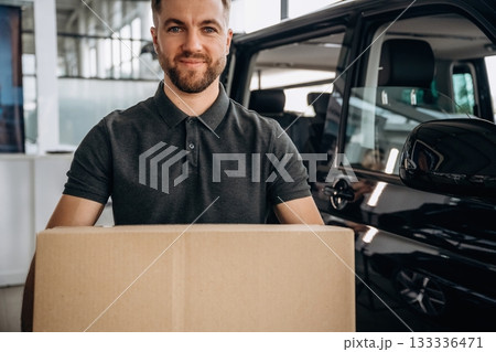 Big order, holding the box. Delivery man or loader is near the car with Big order, holding the box. Delivery man or loader is near the car with 133336471