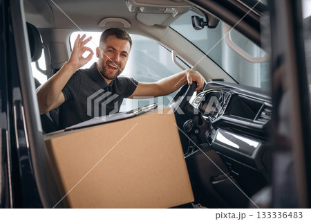 Showing hand gesture, everything is fine, will be done. The delivery man or a loader is in the car with box 133336483