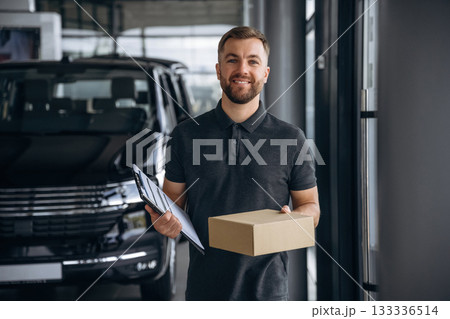 Standing, holding notepad. Delivery man or loader is near the car with a box Standing, holding notepad. Delivery man or loader is near the car with a box 133336514