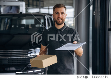 Front view, standing. Delivery man or loader is near the car with a box Front view, standing. Delivery man or loader is near the car with a box 133336519
