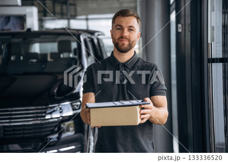 Front view, standing. Delivery man or loader is near the car with a box Front view, standing. Delivery man or loader is near the car with a box 133336520