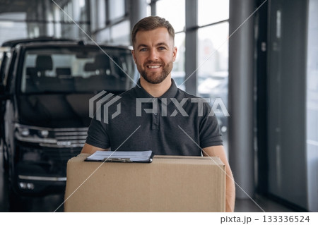 Smiling, positive facial expression. Delivery man or loader is near the car with a box Smiling, positive facial expression. Delivery man or loader is near the car with a box 133336524