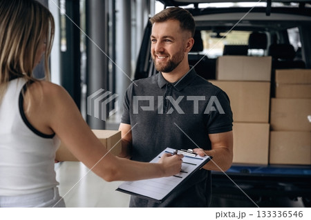 View from the back of female. Woman is taking her order from delivery man, with the car View from the back of female. Woman is taking her order from delivery man, with the car 133336546