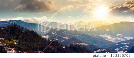panorama of rolling hills and mountain ridge with snow cowered tops at sunset. beautiful landscape in springtime cold weather in evening light. timeless nostalgia book cover with rainbow panorama of rolling hills and mountain ridge with snow cowered tops at sunset. beautiful landscape in springtime cold weather in evening light. timeless nostalgia book cover with rainbow 133336705
