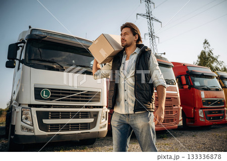 Delivery is on the way, with box. Truck driver is near the transport outdoors Delivery is on the way, with box. Truck driver is near the transport outdoors 133336878