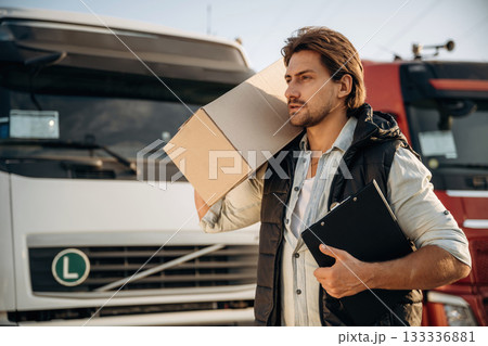 Shipping conception, with box. Truck driver is near the transport outdoors Shipping conception, with box. Truck driver is near the transport outdoors 133336881