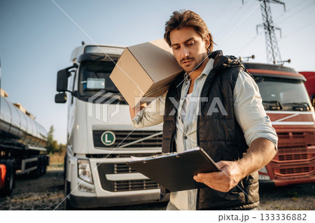 Shipping conception, with box. Truck driver is near the transport outdoors Shipping conception, with box. Truck driver is near the transport outdoors 133336882