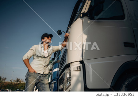 Front view, leaning on the cabin. Truck driver is near the transport outdoors Front view, leaning on the cabin. Truck driver is near the transport outdoors 133336953