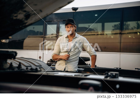 Looking at the truck, smoking. Driver is near the transport outdoors Looking at the truck, smoking. Driver is near the transport outdoors 133336975