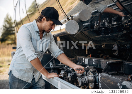In shirt and in a cap. Truck driver is near the transport outdoors In shirt and in a cap. Truck driver is near the transport outdoors 133336983
