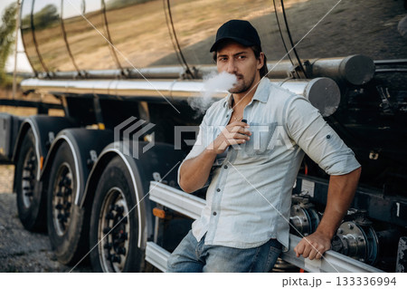 Smoking the electronic cigarette, vape. Truck driver is near the transport outdoors Smoking the electronic cigarette, vape. Truck driver is near the transport outdoors 133336994
