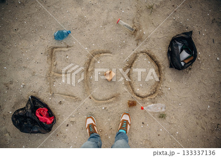 Top view of sand with word eco, trash on the ground, legs of the person 133337136