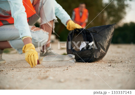 Picking up the bottle. A volunteers collects garbage on a muddy beach 133337143